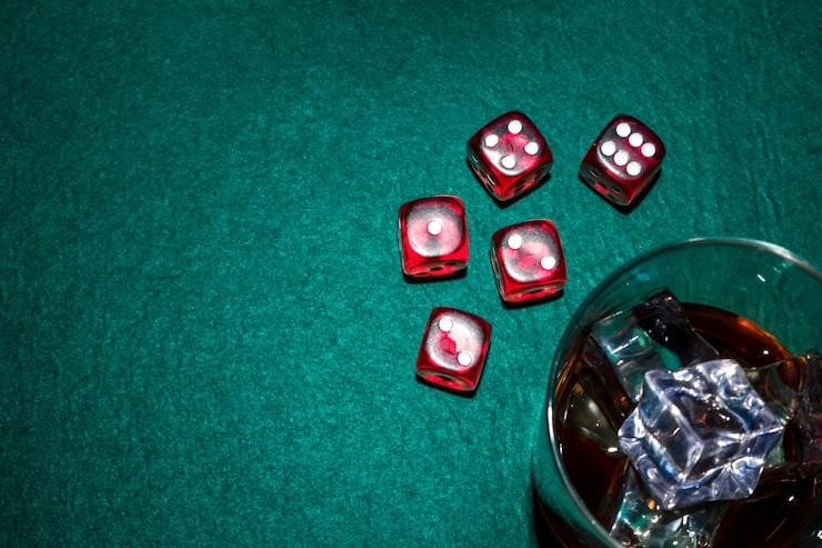 Red dices and whiskey glass with ice cubes on poker table